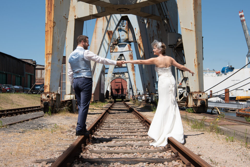 Das Brautpaar balanciert auf Industrieschienen im Hamburger Hafen und fasst sich dabei an die Hände
Hochzeitsfotografen