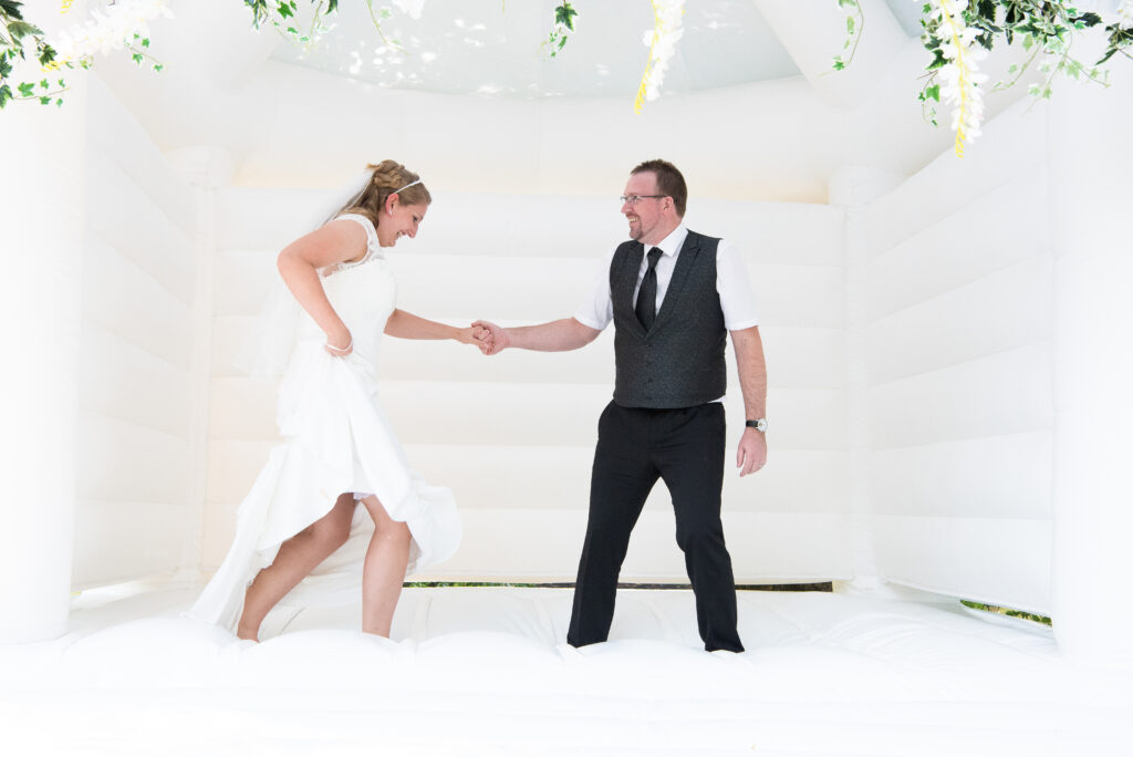 Hand in Hand springt ein Brautpaar durch eine weiße Hüpfburg
Hochzeitsfotografen